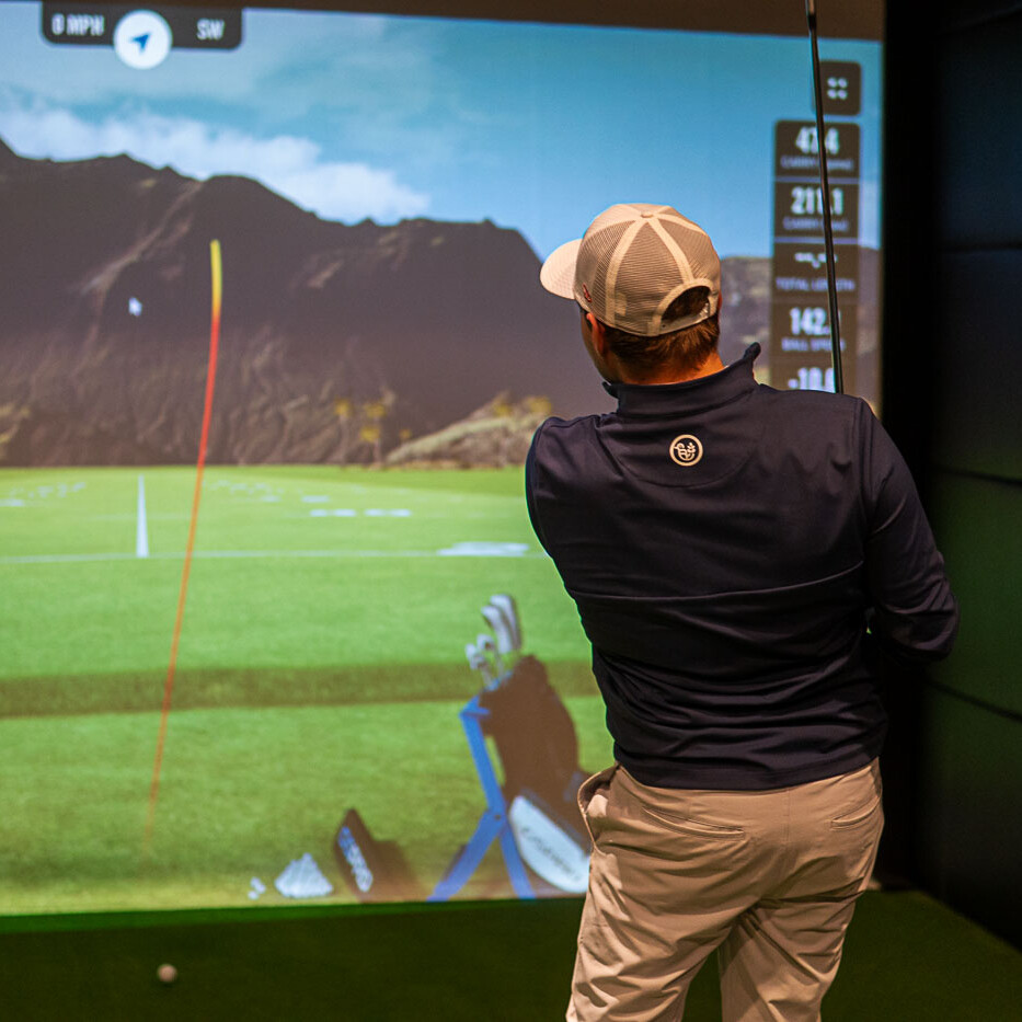 Golfer Finishes Shot in Front of a Indoor Golf Simulator Screen