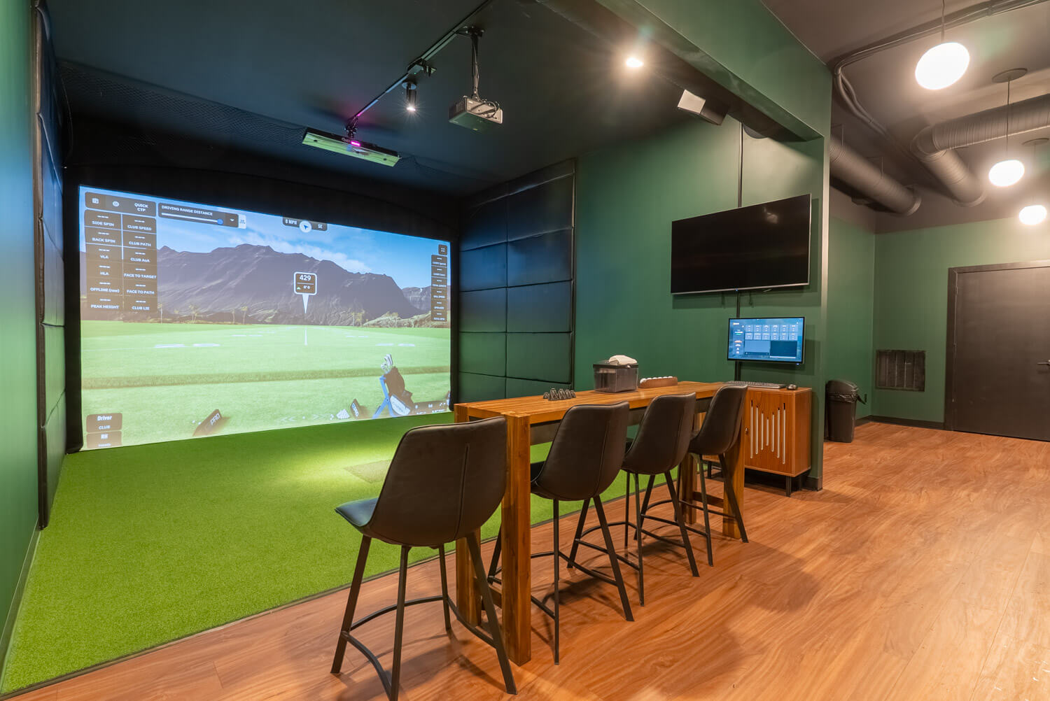 Indoor golf simulator bay with chairs and table in front